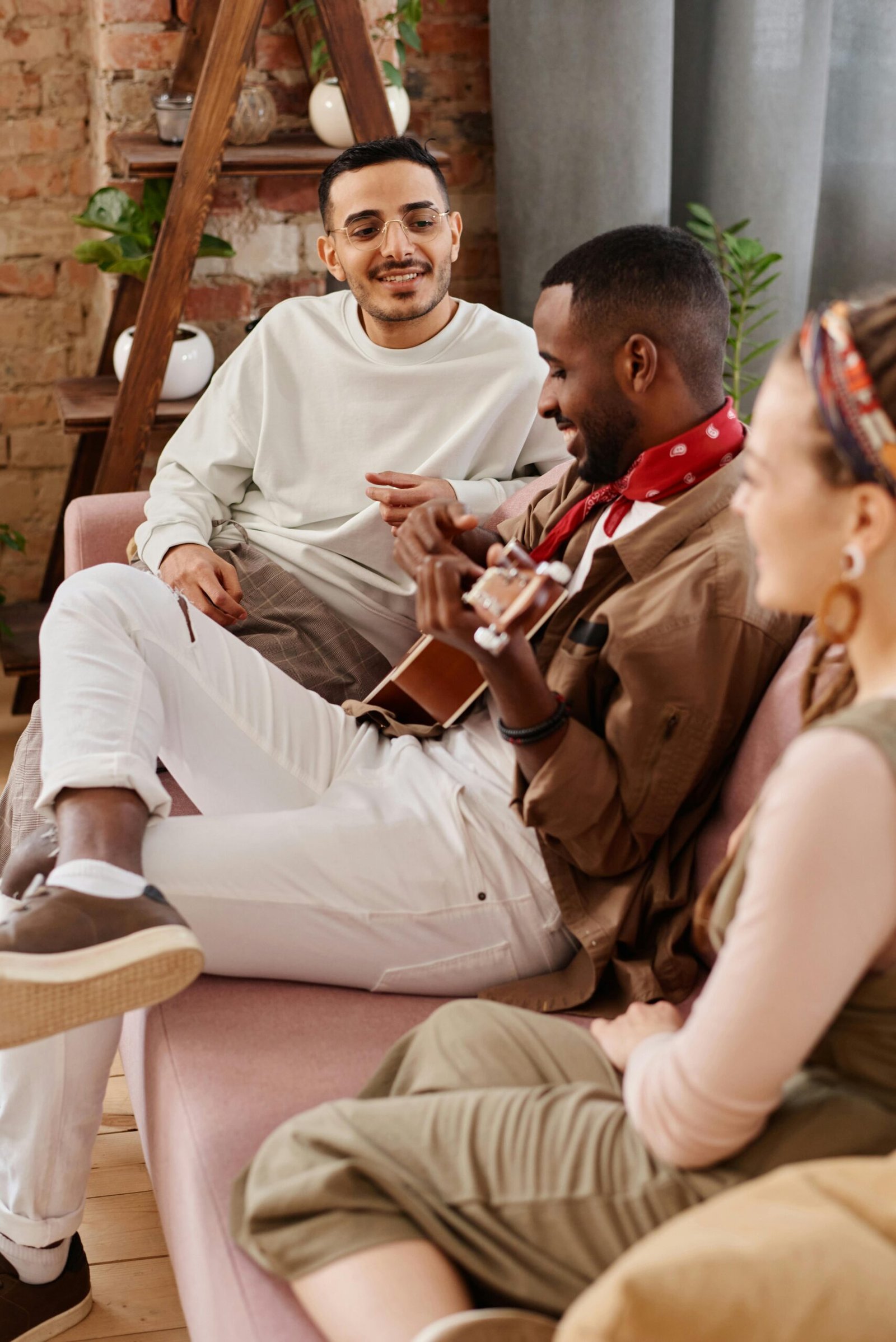 A diverse group of friends enjoying music and bonding over an acoustic guitar indoors.